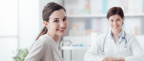 Smiling patient receiving a medical consultation and looking at camera, the female doctor is sitting at desk on the background